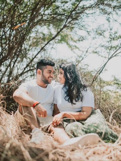 A candid moment of a couple sharing a look while sitting together in a rustic, natural setting. The warm sunlight filtering through the trees adds a beautiful, romantic glow to this outdoor pre-wedding photo.