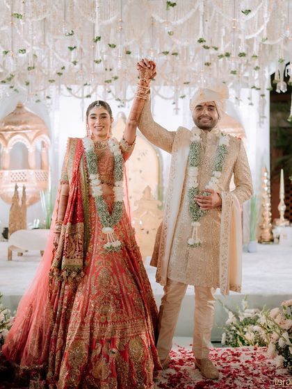 Just married. The triumphant moment after the Varmala, with the couple standing tall under a canopy of white flowers against a beautifully detailed backdrop we designed for their special day.