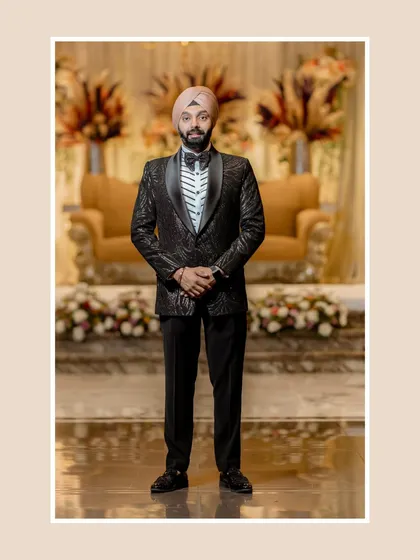 A full-length portrait of the groom, Sanjit, showcasing his textured black tuxedo and poised stance.