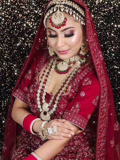 A bride in a deep red lehenga, wearing a matching red-beaded Kundan set. The layered necklace adds to the grandeur.