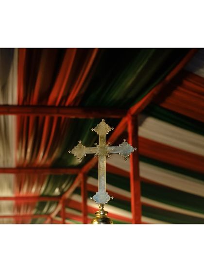 A close-up of a golden cross against the red, white, and green draped ceiling of the Christmas pandal.
