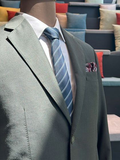 A detailed shot of a finished suit jacket on display at the BCG trunk show. The olive green fabric, paired with a striped blue tie and a subtle pocket square, demonstrates a sophisticated approach to modern business attire.