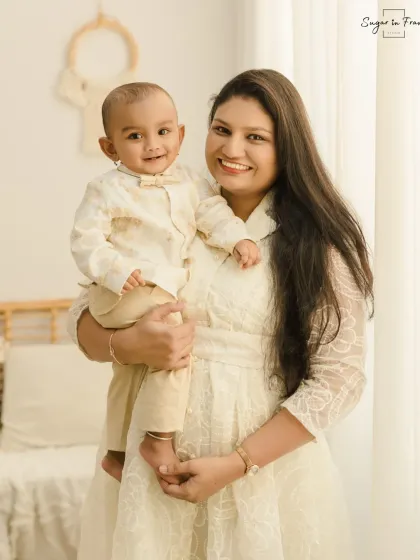 A beautiful mother and son portrait. The mother holds her smiling baby boy, both dressed in light colors that complement the bright and airy feel of the studio.