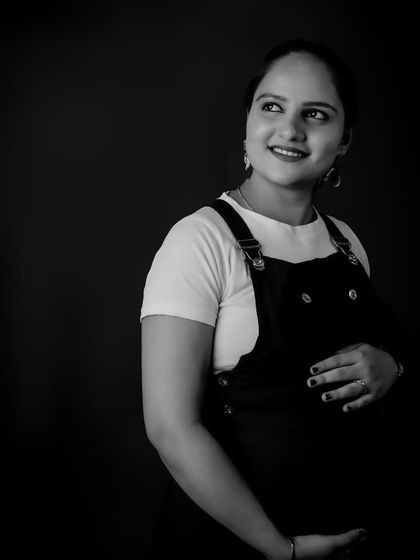 A beautiful black-and-white solo portrait. The lighting is sculpted to highlight the contours of the baby bump and the mom-to-be's serene expression.