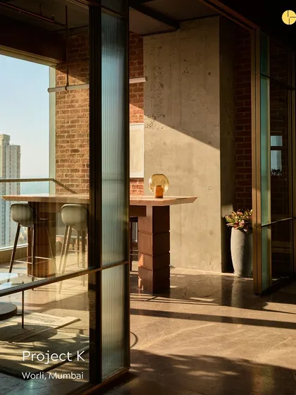 A meeting space in 'Project K,' designed for a private equity firm. The room features a high table overlooking the city, with exposed brick and concrete creating a modern industrial aesthetic that reflects the firm's rooted ideals.