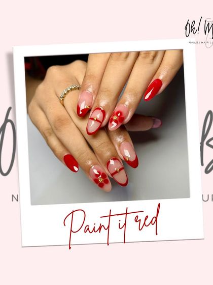 A modern twist on classic red nails, perfect for any party. This design features a negative space look with red tips, a delicate red band, and a small gold floral charm.