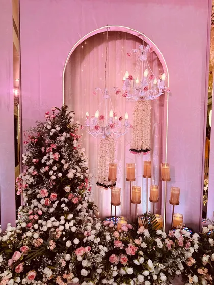 A close-up of a decor element for a pastel-themed event. This setup combines a floral arrangement with a delicate chandelier and candle stands, creating a romantic and intricate corner.