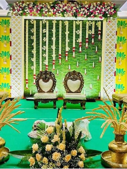 A unique stage setup for a pooja or ceremony, featuring a backdrop with traditional paddy (nel kathir) arrangements. The decor uses brass elements and lotus motifs for an authentic feel.
