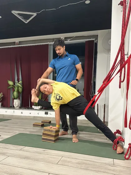 In my classes, I provide hands-on adjustments to ensure your alignment is precise and safe. Here, I am guiding a student in Utthita Parsvakonasana using a rope wall. This support helps stabilize the femur and deepen the pose with intelligence, preventing strain and enhancing body awareness.