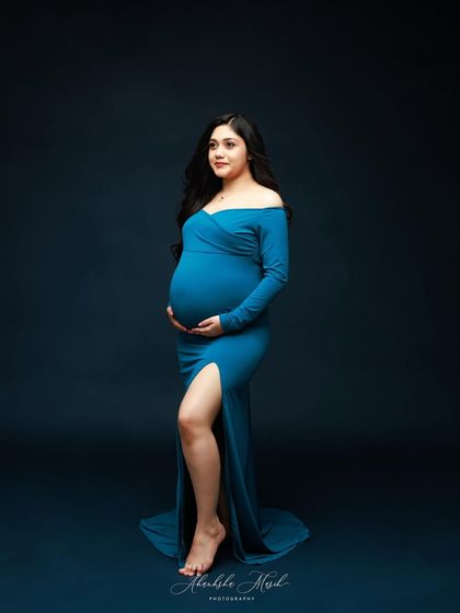 A classic portrait against a deep blue backdrop, this shot highlights the beautiful fit of the teal gown and the mother's serene expression.