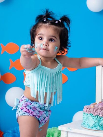 Offering a piece of cake to the camera. The interactive and playful nature of one year olds makes for such dynamic and engaging photographs.