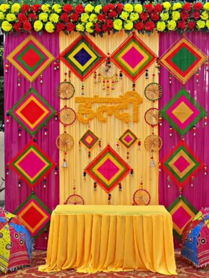 Here is a vibrant Haldi ceremony backdrop, bursting with color. I used traditional elements like Rajasthani umbrellas, colorful kite-shaped hangings, and a mix of real and artificial flowers to create a truly festive atmosphere for this outdoor event.