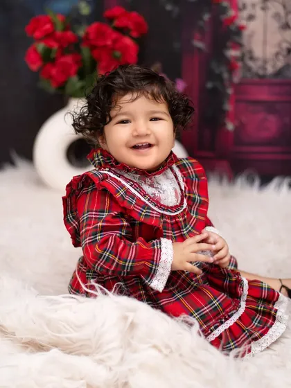 A bright smile in a beautiful red dress. This little girl's happiness shines in our romantic red rose themed setup, creating a classic and heartwarming portrait.