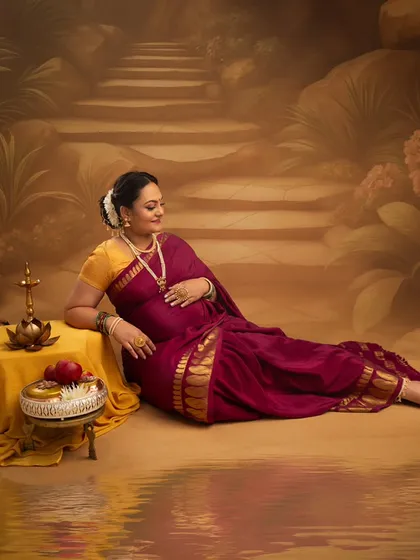 Reclining gracefully by the water's edge, this mother-to-be is a picture of tranquility. The traditional lamp and offering of fruit add to the serene, painterly quality of the portrait.