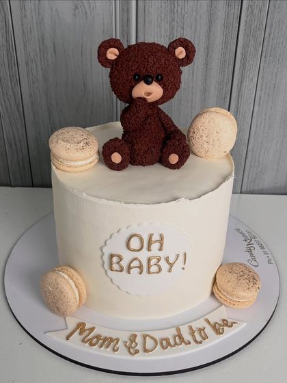 A simple and elegant "Oh Baby!" cake for a baby shower. This design features a textured teddy bear topper and is accented with delicious macarons, perfect for celebrating the mom and dad-to-be.