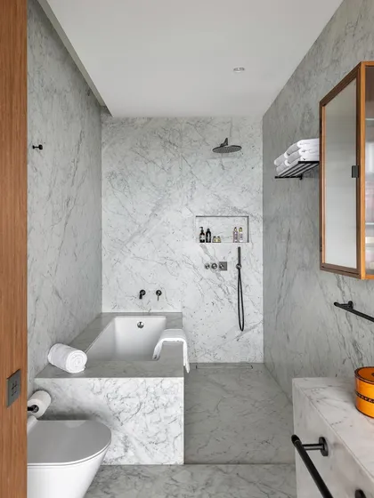 The bathroom in the Worli Duplex is clad in white Carrara marble, creating a serene and monolithic space. The minimal palette is complemented by fluted wood accents, ensuring visual continuity with the rest of the home.