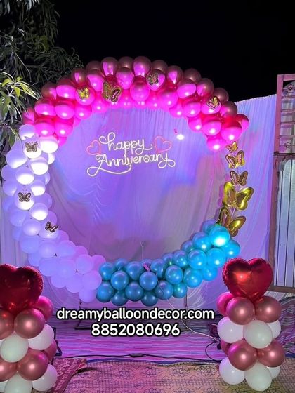 A beautiful anniversary decoration for an outdoor or evening event. The balloon ring features a gradient of colors and is decorated with butterfly accents and a neon sign.