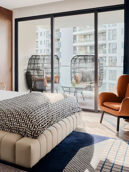 The bedroom opens onto a private balcony with comfortable seating, perfect for enjoying the Bangalore weather. The natural light floods the room, highlighting the mix of textures and patterns.