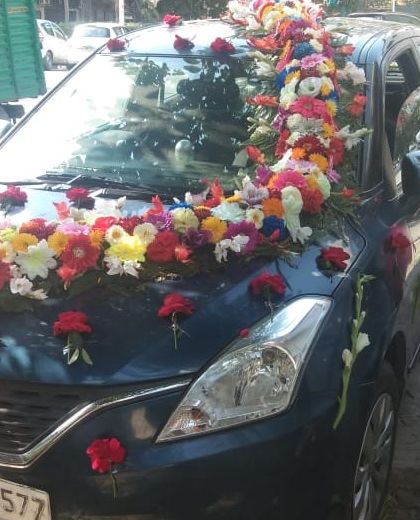 A vibrant and colorful decoration for a blue Maruti Suzuki Baleno. The mix of many different flowers creates a joyful and celebratory look.