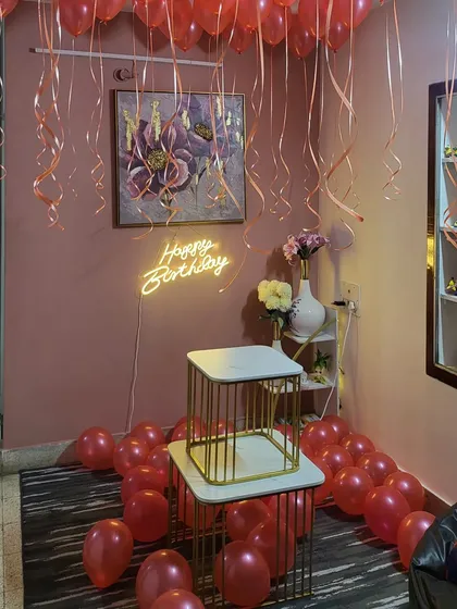 A simple and romantic room decoration with red helium balloons and a 'Happy Birthday' neon sign.