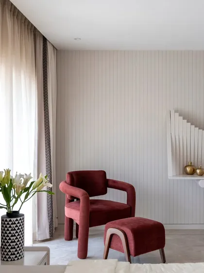 A detail shot from the parent's bedroom, featuring a plush burgundy armchair and ottoman. This cozy reading corner is set against a wall with subtle vertical paneling, adding texture and a sense of height to the room.