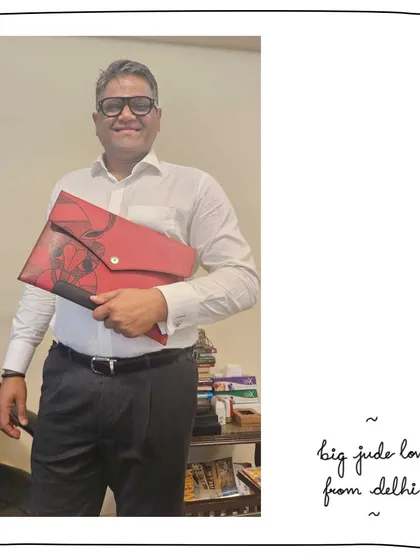 A great gift for our patron Meghana's husband. He's holding the Big Jude folio clutch, customized with a vibrant Gond art motif on Cranberry red leather. It's a bold and artistic statement piece.