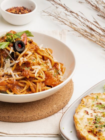 A bowl of my spaghetti bolognese, rich with meaty tomato sauce and topped with parmesan, served with a side of cheesy garlic bread.