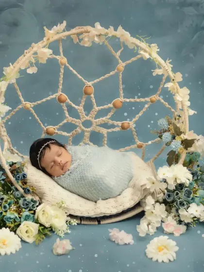 This wider shot shows the full dreamcatcher setup, with the baby girl nestled among soft blue and white flowers.