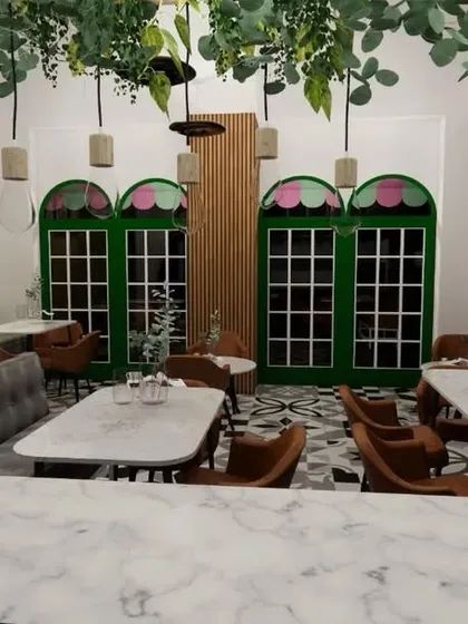 This final view from behind the main counter shows the full scope of the cafe's interior. The design uses hanging plants and pendant lights to draw the eye upwards and make the space feel larger, while the marble counter adds a touch of elegance.