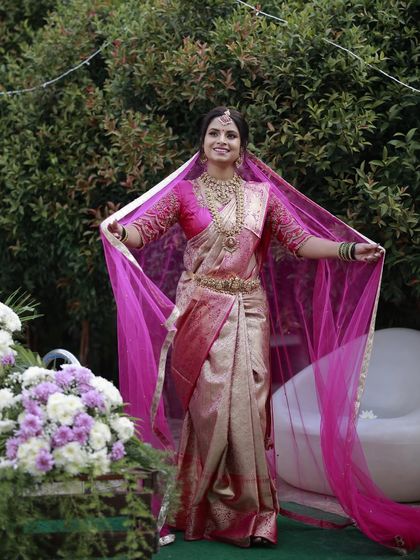 A full-length shot of Madhurya, showing how the complete look comes together with her stunning pink saree and veil. The makeup is designed to be radiant and photogenic.