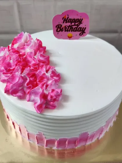 A simple round birthday cake with white and pink frosting. The ruffled pink flowers on top add a pop of color and texture.