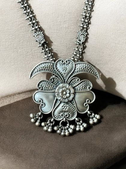 An antique and statement oxidised silver pendant. The floral-shaped pendant has a beautiful, three-dimensional quality and delicate ghungroo drops.