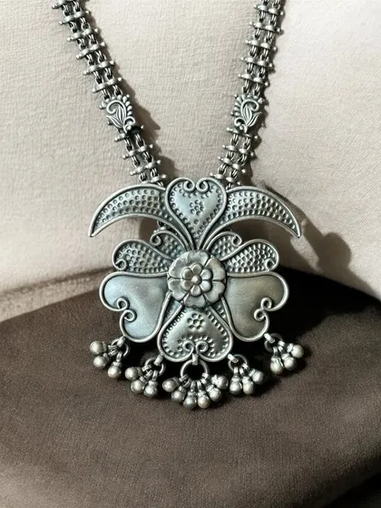 An antique and statement oxidised silver pendant. The floral-shaped pendant has a beautiful, three-dimensional quality and delicate ghungroo drops.