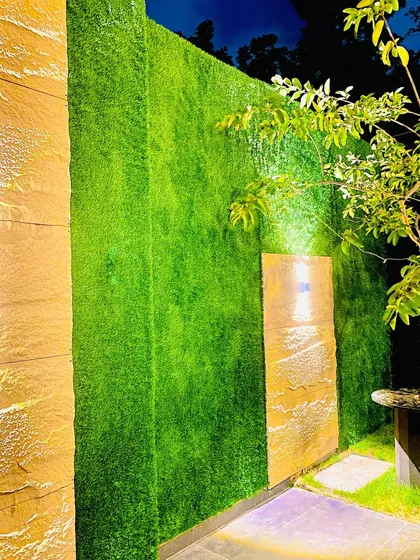 Artificial turf is not just for floors. Here, we used it to create a striking green feature wall, accentuated with warm lighting for a dramatic evening look. This adds texture and a unique design element to an exterior wall.