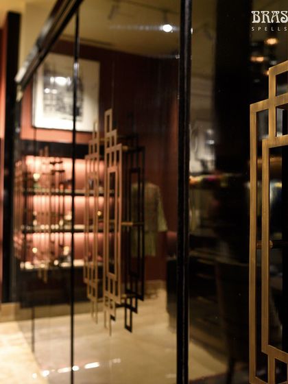 The warm glow of the brass handles is reflected in the glass and polished surfaces of the JJ Valaya store. This view shows how the hardware interacts with its environment, contributing to the rich, layered aesthetic of the interior.