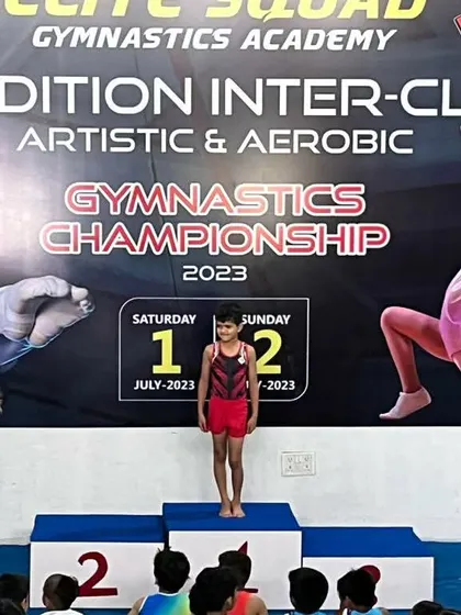 A young gymnast standing proudly on the winner's podium. This is a moment of immense pride for the student, coaches, and parents.