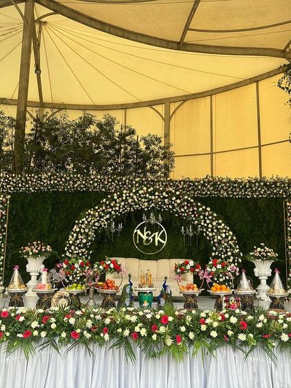 A beautiful tented wedding setup with a green hedge backdrop and a floral arch featuring a custom monogram.