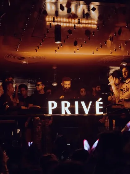 The "PRIVÉ" sign glowing in the dark, with the crowd visible in the background. This shot captures the exclusive, high-energy vibe of the afterparty.
