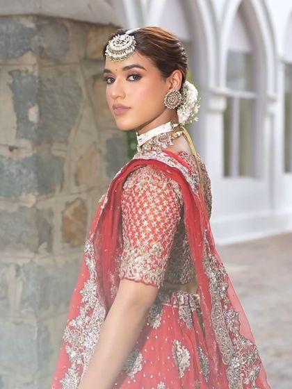 A classic red bridal lehenga with intricate silver embroidery. The look is completed with a sleek bun, fresh flowers, and traditional jewelry.