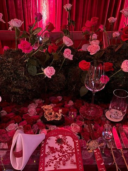 The interplay of textures on the table is key to this design. The soft rose petals contrast with the earthy moss runner, the smooth glass, and the delicate paper of the place cards, creating a rich sensory experience.