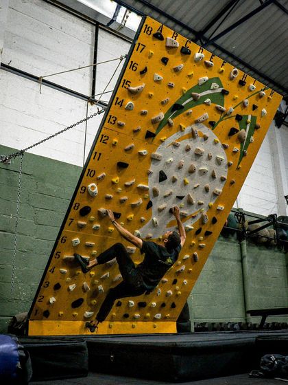 A climber executes a powerful move on the MoonBoard. The steep angle and small holds are designed to build serious finger strength and core stability for advanced rock climbing.