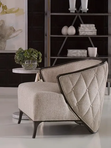 This graceful lounge chair features curving, wing-like arms that are buttoned and tufted on the outside. Trimmed in dark wood, the chair's unique silhouette makes it a sculptural and comfortable addition to any room.