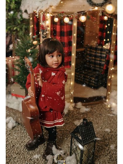 A portrait of the little girl holding a guitar in the middle of our snowy, light-filled set.