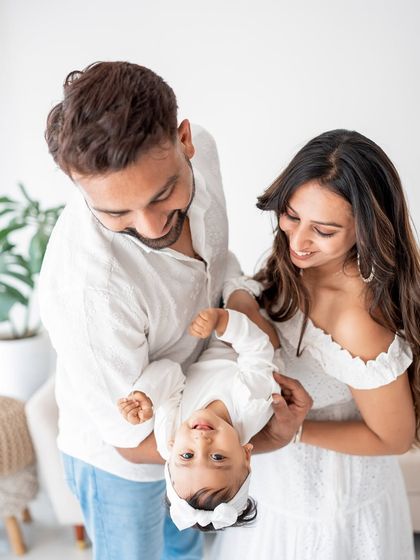 A family playing with their baby, holding her upside down for a giggle.