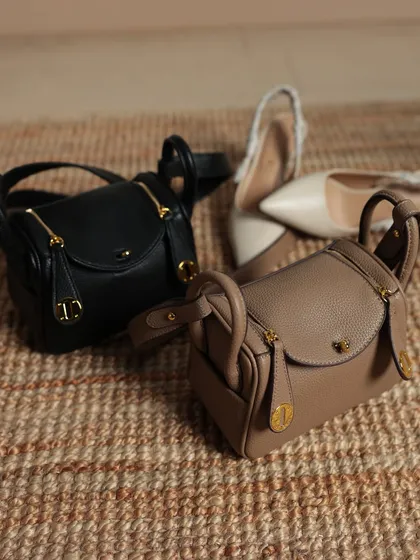 The Linde Mini bags in black and taupe, placed next to a pair of elegant heels. This flat lay shows the fine details like the zipper pulls and the structured handles.