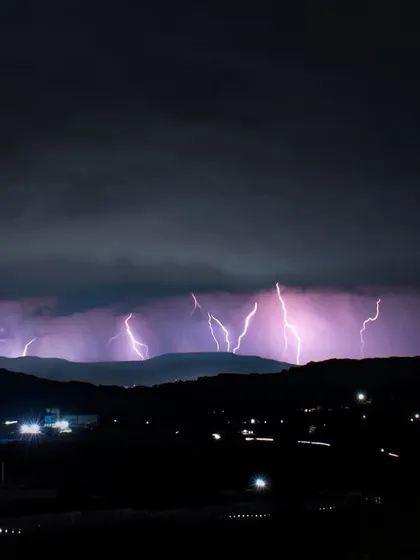 A wide shot captures an entire range of hills in Pune being lit up by a series of powerful lightning strikes.