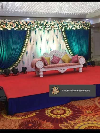 A unique stage design using a combination of deep teal and white drapes. The floral arrangements on top and the colorful cushions add a touch of vibrancy to this elegant reception setup.