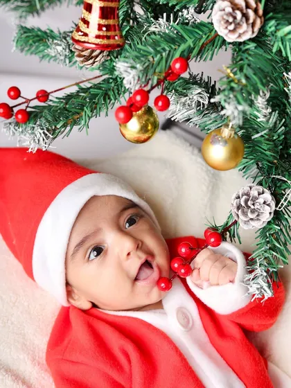 This curious baby in a Santa suit reaches for the ornaments on a miniature Christmas tree.