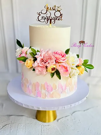 Soft pastels, fresh florals, and a little gold sparkle make this two-tier cake the sweetest way to say 'Just Engaged'. The bottom tier features a beautiful palette knife painted texture.