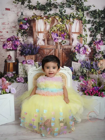 A joyful, full-width shot of the birthday girl in her pastel rainbow dress, seated happily in her secret garden setup.